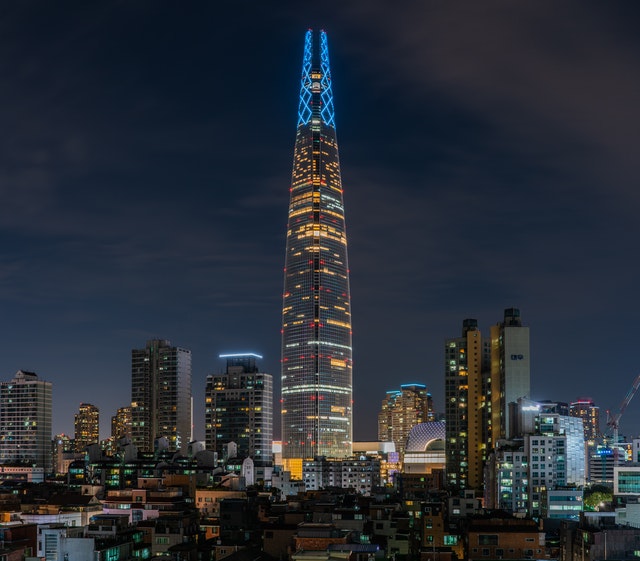 Image of a tower thats taller then all the others around it, very modern and lit up contrasting with night sky